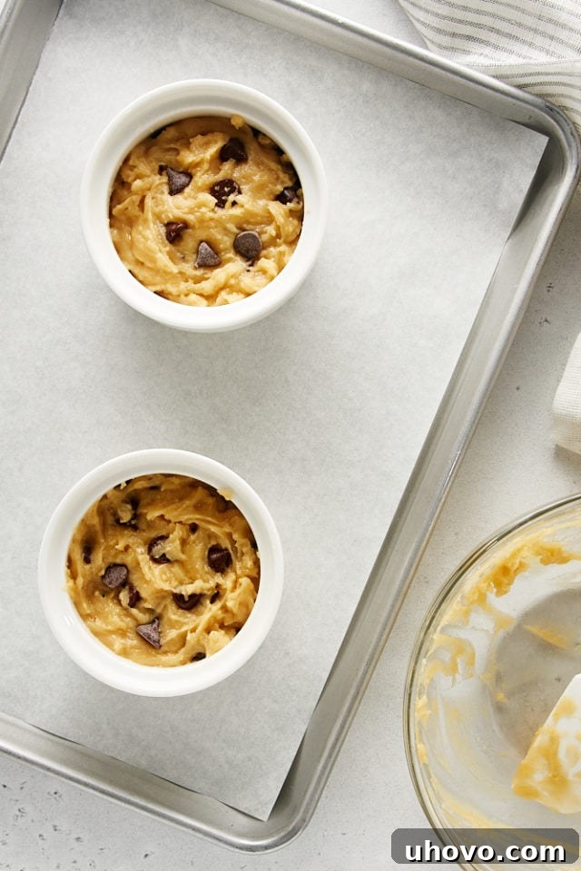 Two Deep Dish Chocolate Chip Cookies, unbaked and perfectly portioned, resting in white ramekins on a baking sheet, poised for their journey into the oven.