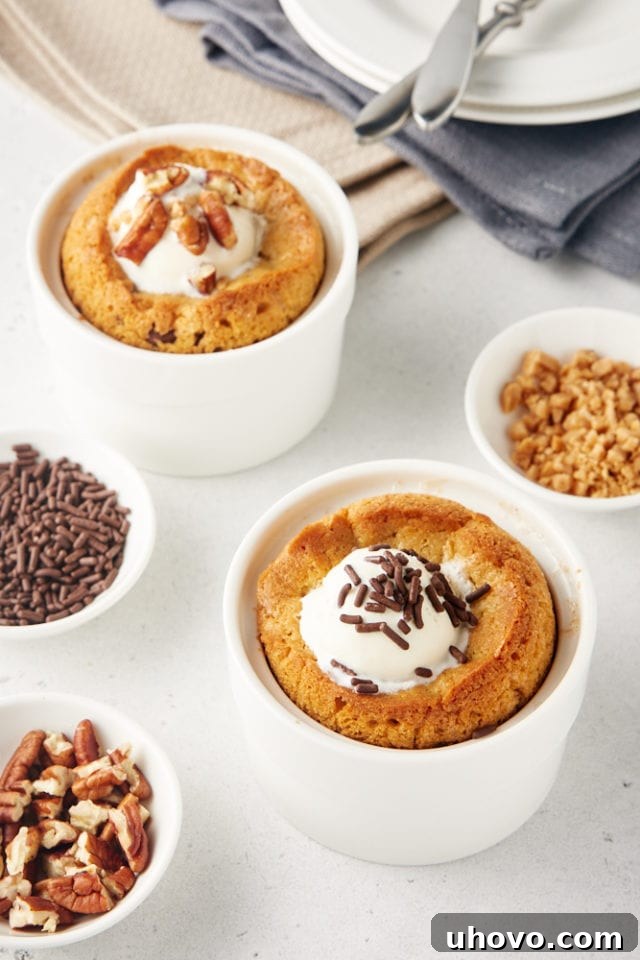 A Deep Dish Chocolate Chip Cookie for Two, generously topped with a scoop of melting ice cream, a sprinkle of crunchy nuts, and colorful sprinkles, ready for immediate enjoyment.