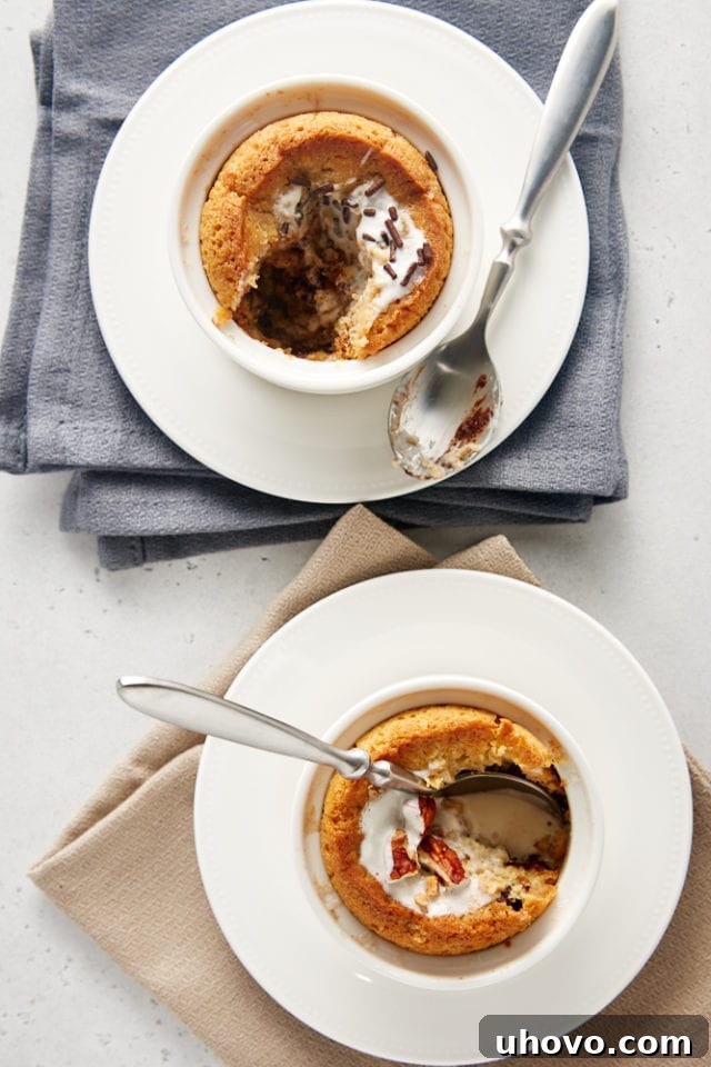 Overhead view of two perfectly baked Deep Dish Chocolate Chip Cookies for Two, served in elegant white ramekins on pristine white plates with stylish gray and beige napkins underneath, ready to be enjoyed.