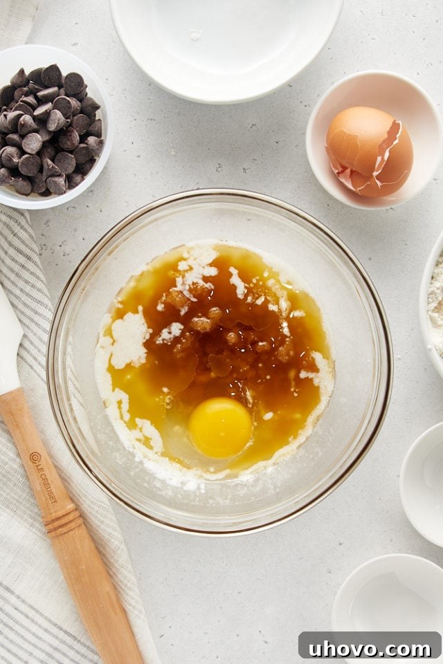 Brown sugar, a fresh egg, and vanilla extract are added to cooled melted butter in a clear glass mixing bowl, initiating the wet ingredients mixture for Deep Dish Chocolate Chip Cookies.