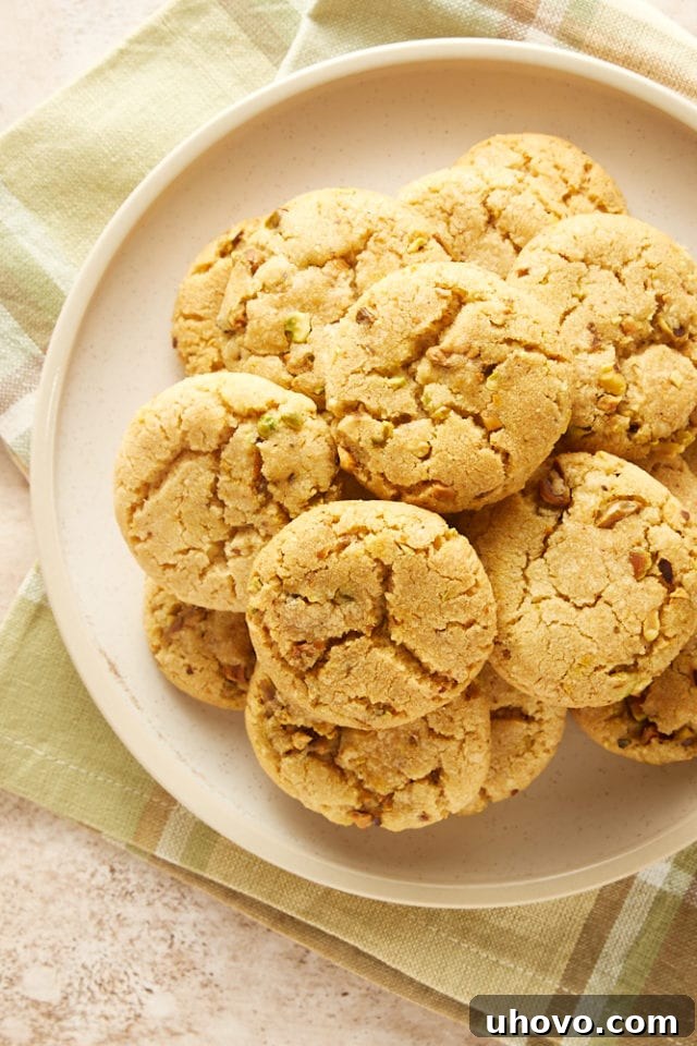 Delicious Brown Butter Pistachio Cookies piled elegantly on a beige plate, showcasing their inviting texture and golden-brown edges.
