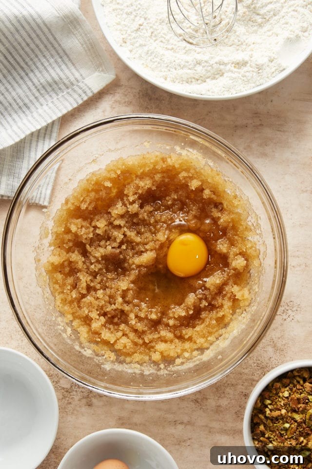 The egg, vanilla extract, and orange extract are added to the rich brown butter and sugar mixture in a glass bowl, ready to be beaten.