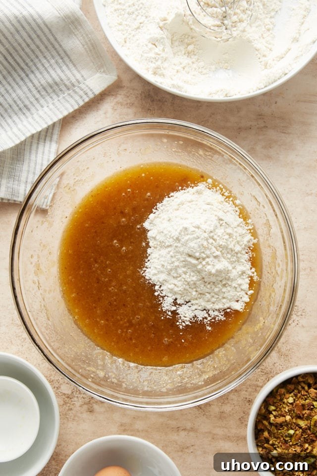 The flour mixture is gradually added to the wet ingredients in a glass mixing bowl, beginning the process of forming the cookie dough.