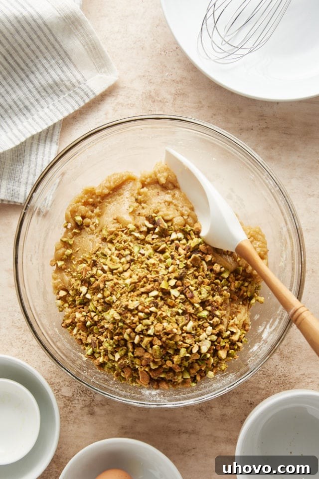 Roughly chopped pistachios are added to the cookie dough in a glass mixing bowl, ready to be folded in.