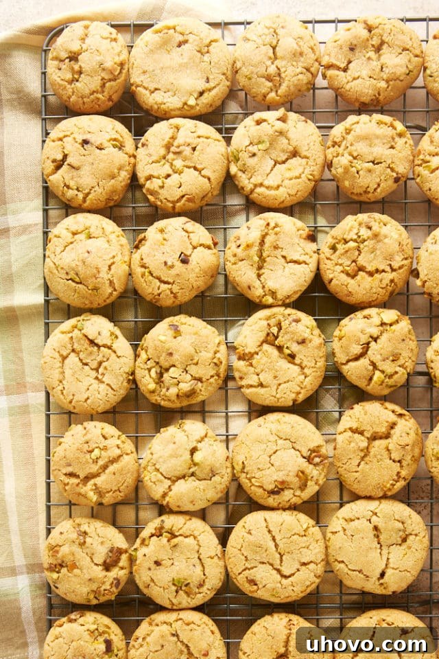 Freshly baked Brown Butter Pistachio Cookies cooling on a wire rack, their golden edges and crackled tops visible and inviting.