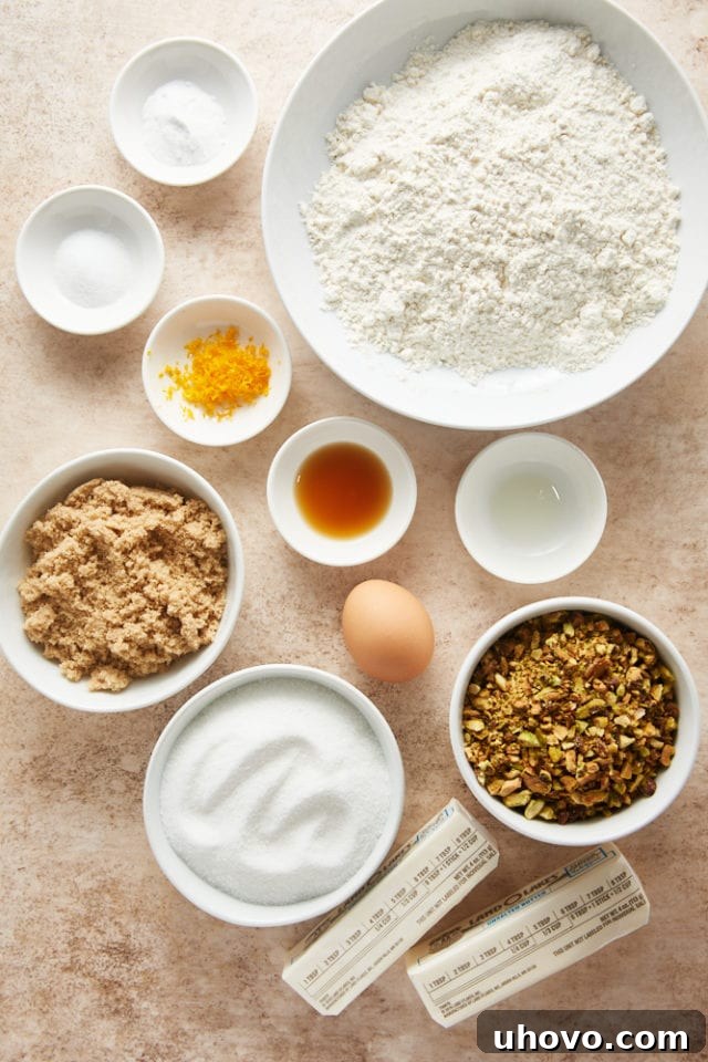 An overhead shot showcasing all the essential ingredients laid out neatly for crafting Brown Butter Pistachio Cookies, highlighting fresh orange and vibrant pistachios.