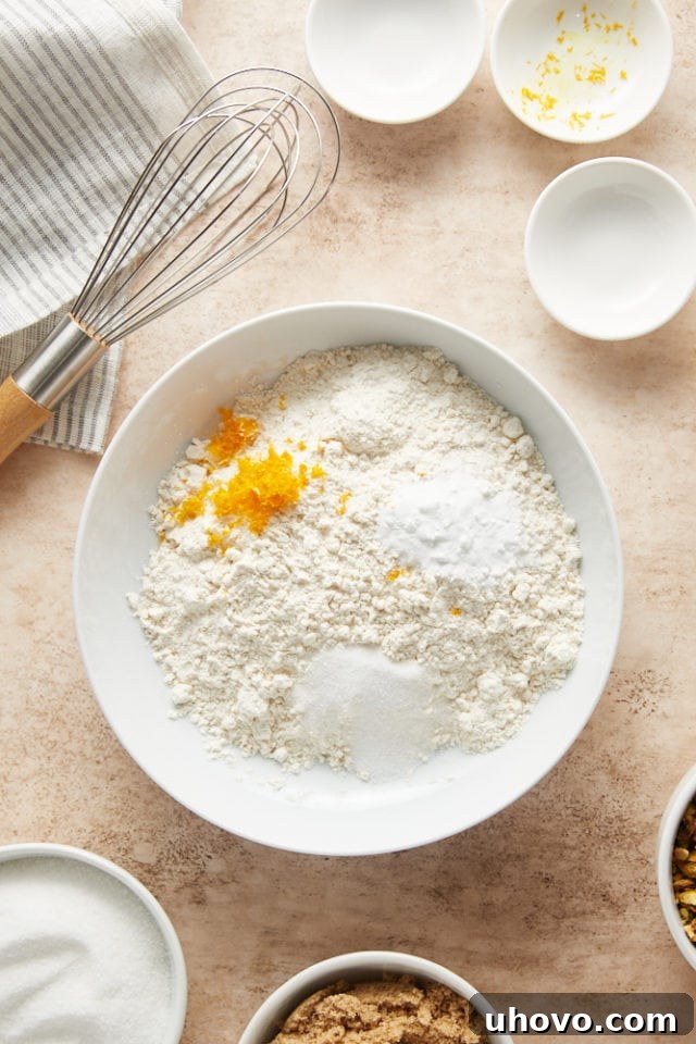 A white bowl holds the dry ingredients: flour, baking soda, salt, and fresh orange zest, waiting to be combined.