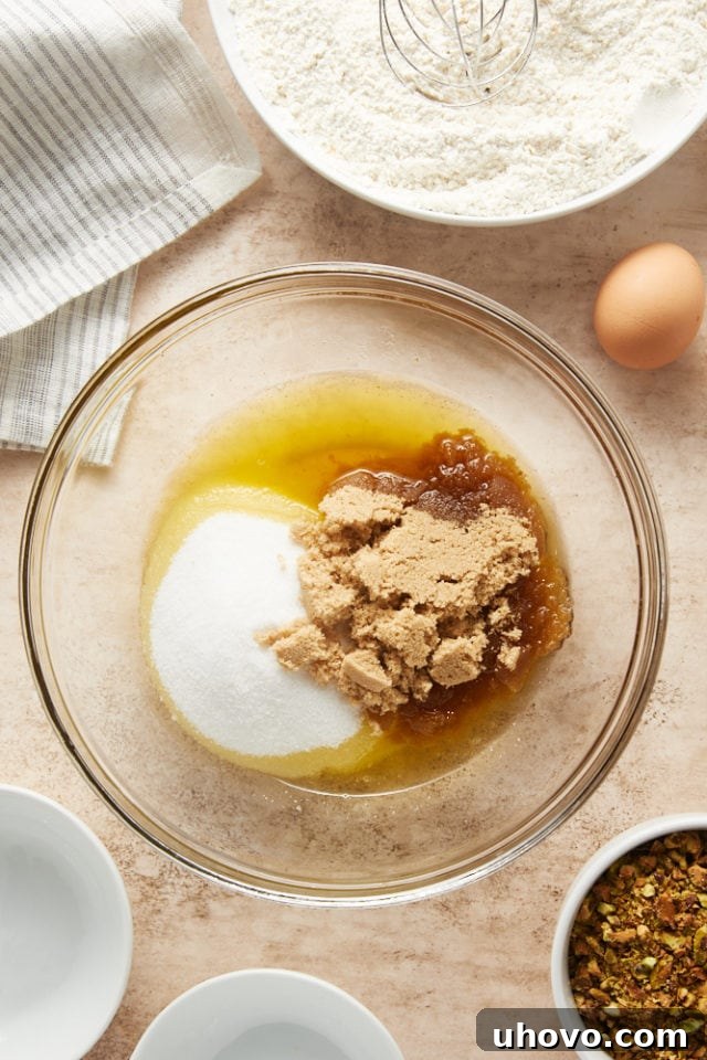 In a glass mixing bowl, cooled brown butter is combined with granulated sugar and brown sugar, ready for mixing.