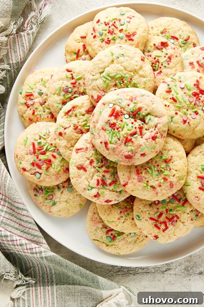 Overhead view of soft Christmas sugar cookies on a large white plate, adorned with festive sprinkles.