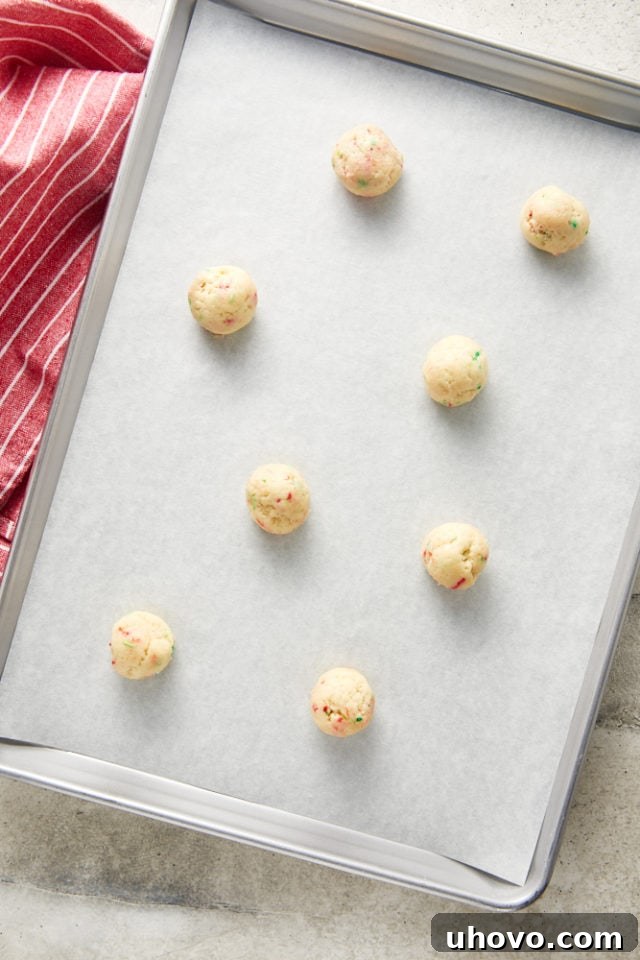 Overhead view of uniformly rolled sugar cookie dough balls placed on a parchment-lined baking sheet.