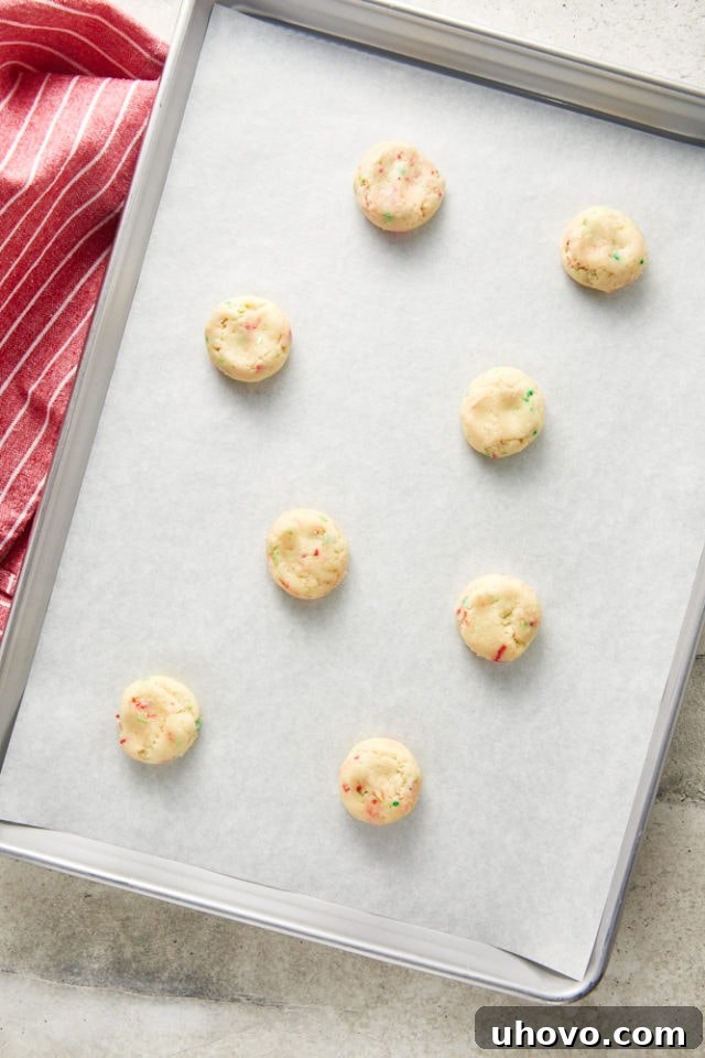 Overhead view of flattened sugar cookie dough balls with additional sprinkles on a parchment-lined baking sheet, ready for baking.