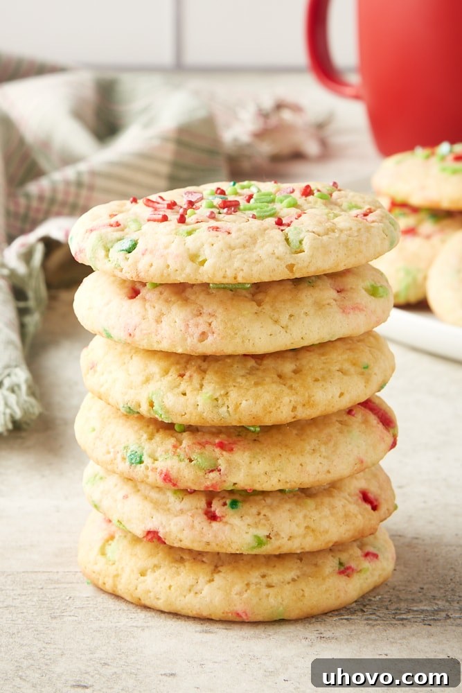A charming stack of soft Christmas sugar cookies, with more cookies and a cozy red mug in the background, creating a festive scene.