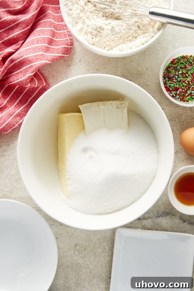 Overhead view of butter, cream cheese, and sugar starting to combine in a white mixing bowl.