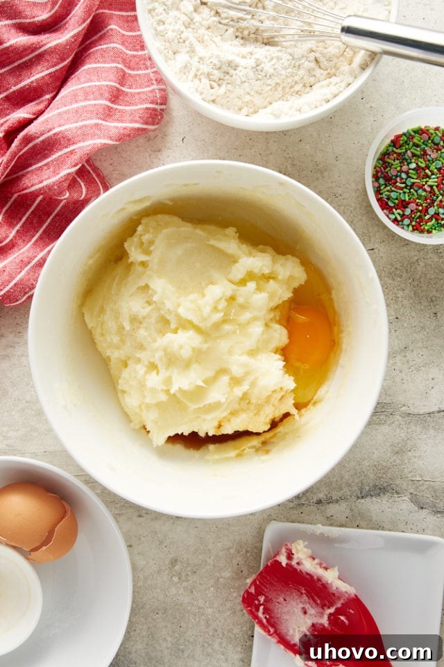 Overhead view of egg and vanilla extract being added to the creamed butter-cream cheese-sugar mixture.