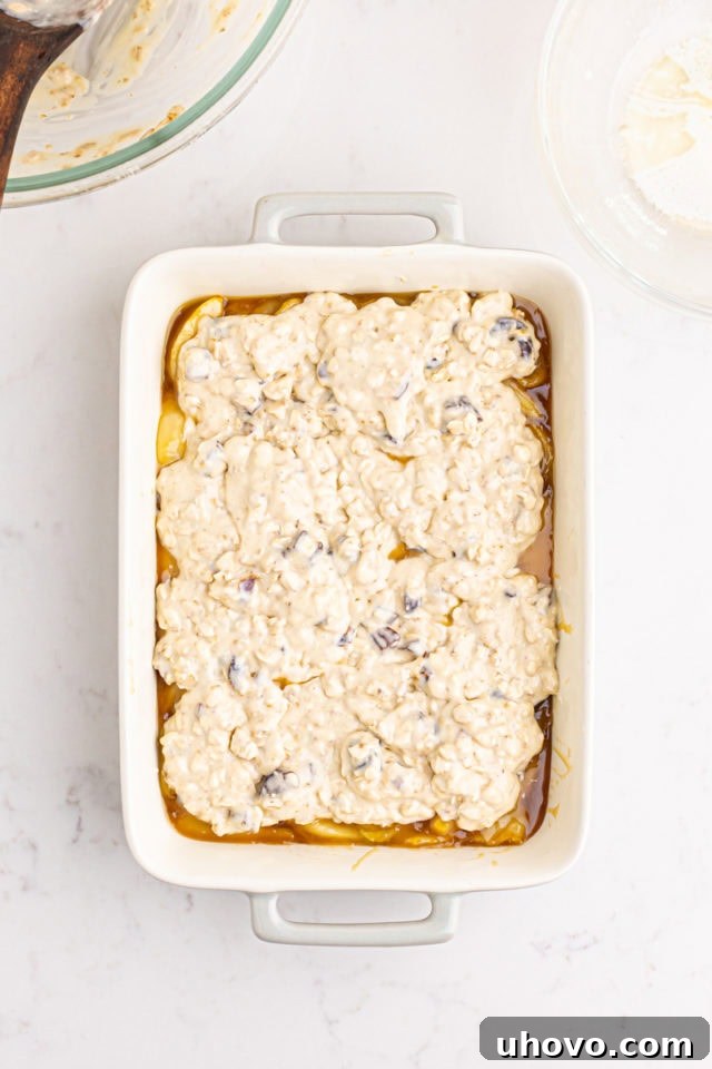 Overhead view of the unbaked caramel apple pear cobbler with the crust mixture spooned over the fruit filling in a rectangular baking pan.