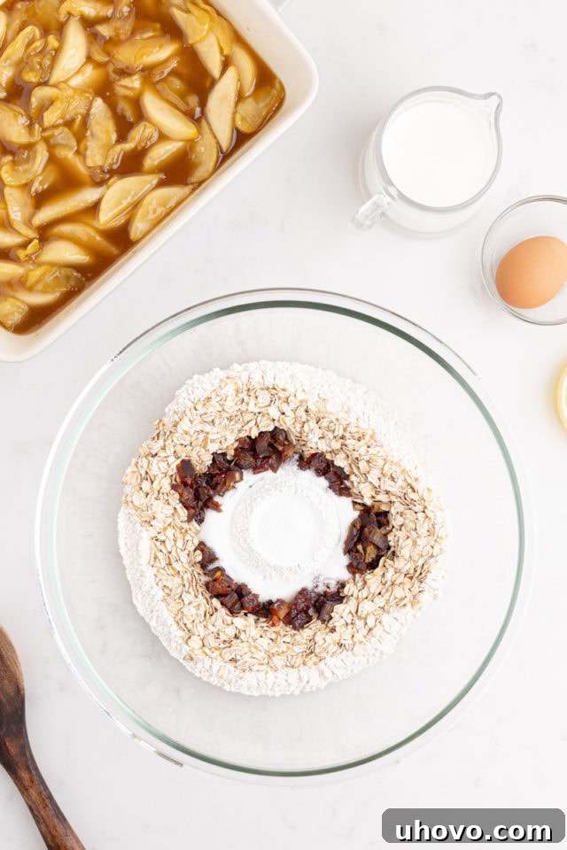Overhead view of dry ingredients for the cobbler topping – flour, oats, dates, baking powder, and salt – combined in a glass mixing bowl.