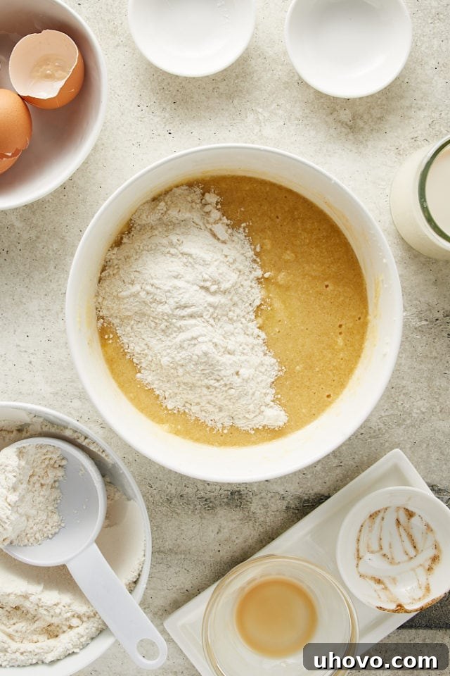Flour being gently added to the wet cake batter in a white mixing bowl, illustrating the careful incorporation of ingredients.