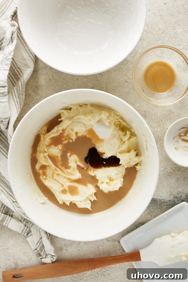 Irish cream liqueur and vanilla bean paste being poured into the butter and sugar mixture, enhancing the frosting's flavor.