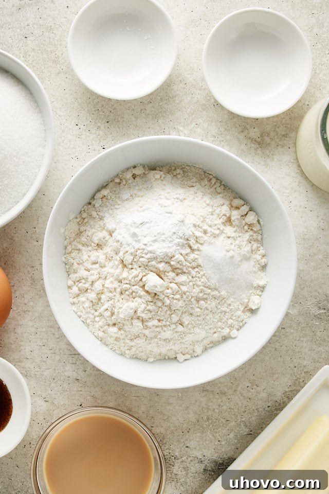 Overhead shot of individual dry ingredients: cake flour, baking powder, and salt, resting in a pristine white mixing bowl.