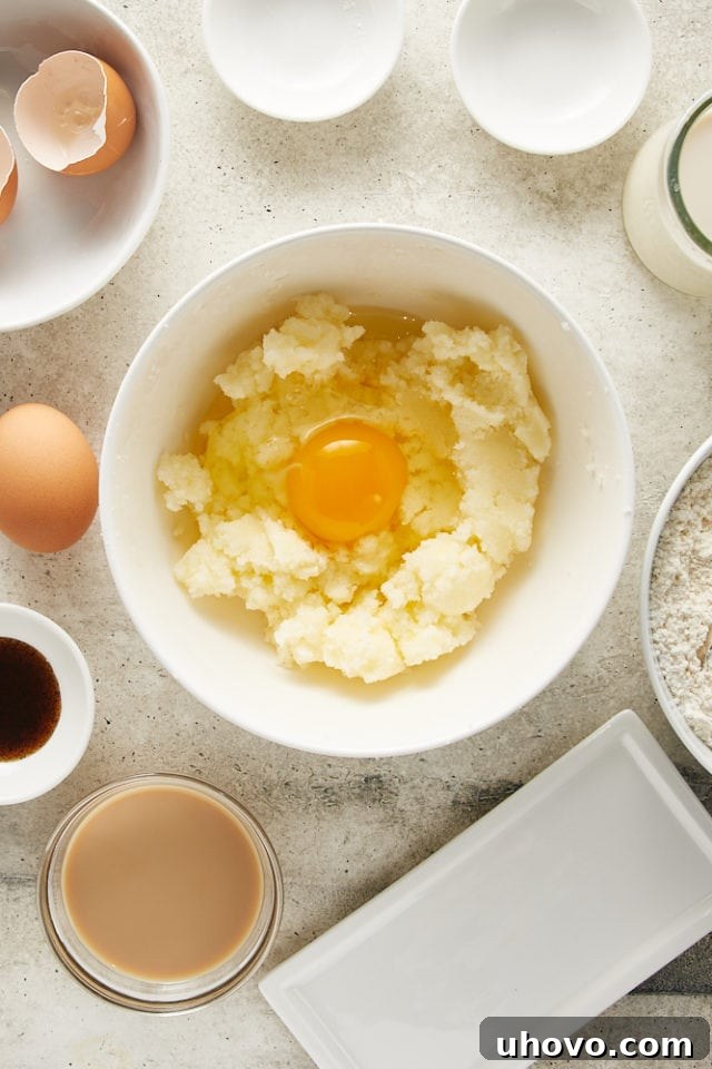 A single egg cracking into the creamy butter and sugar mixture in a white bowl, ready to be incorporated into the cake batter.