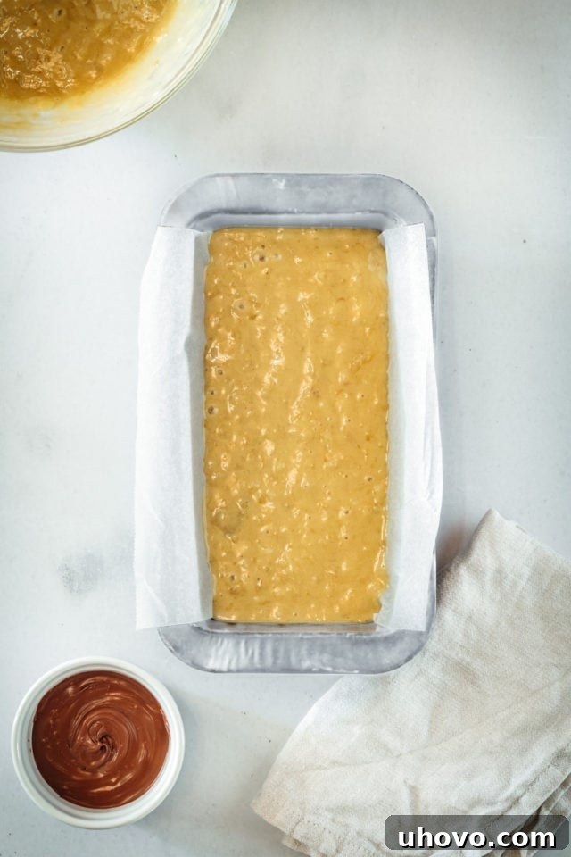 Overhead view of the first half of banana bread batter perfectly poured into a parchment-lined loaf pan, ready for the Nutella layer.