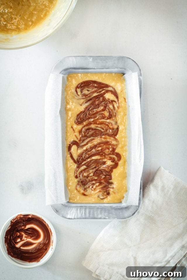 Overhead view after gently swirling Nutella into the banana bread batter with a knife, creating beautiful, distinct chocolate ribbons throughout the first layer of batter.