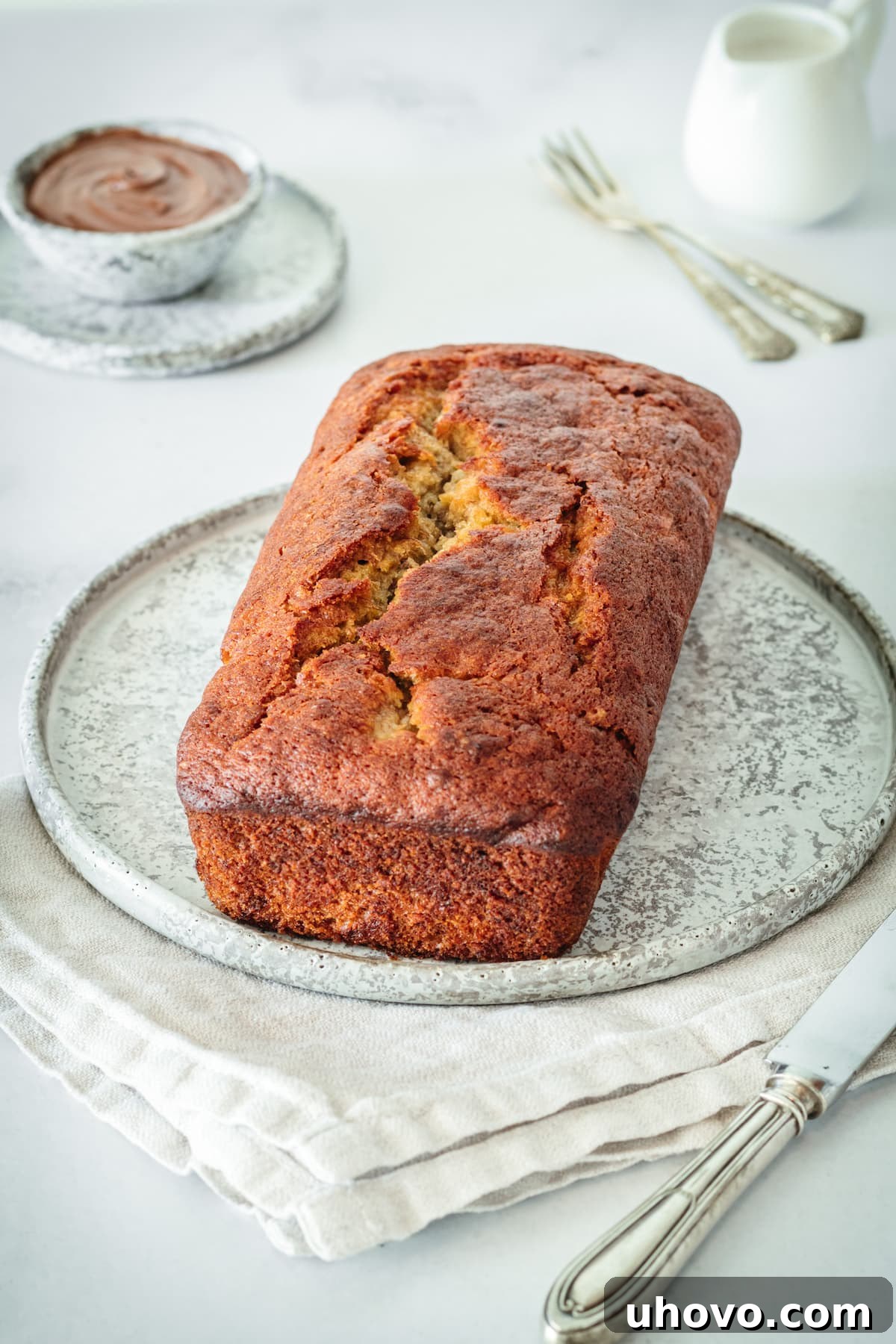 A perfectly baked, golden-brown loaf of Nutella Banana Bread resting on a plate, hot out of the oven, with a delightful crack along the top, before being cut into slices.