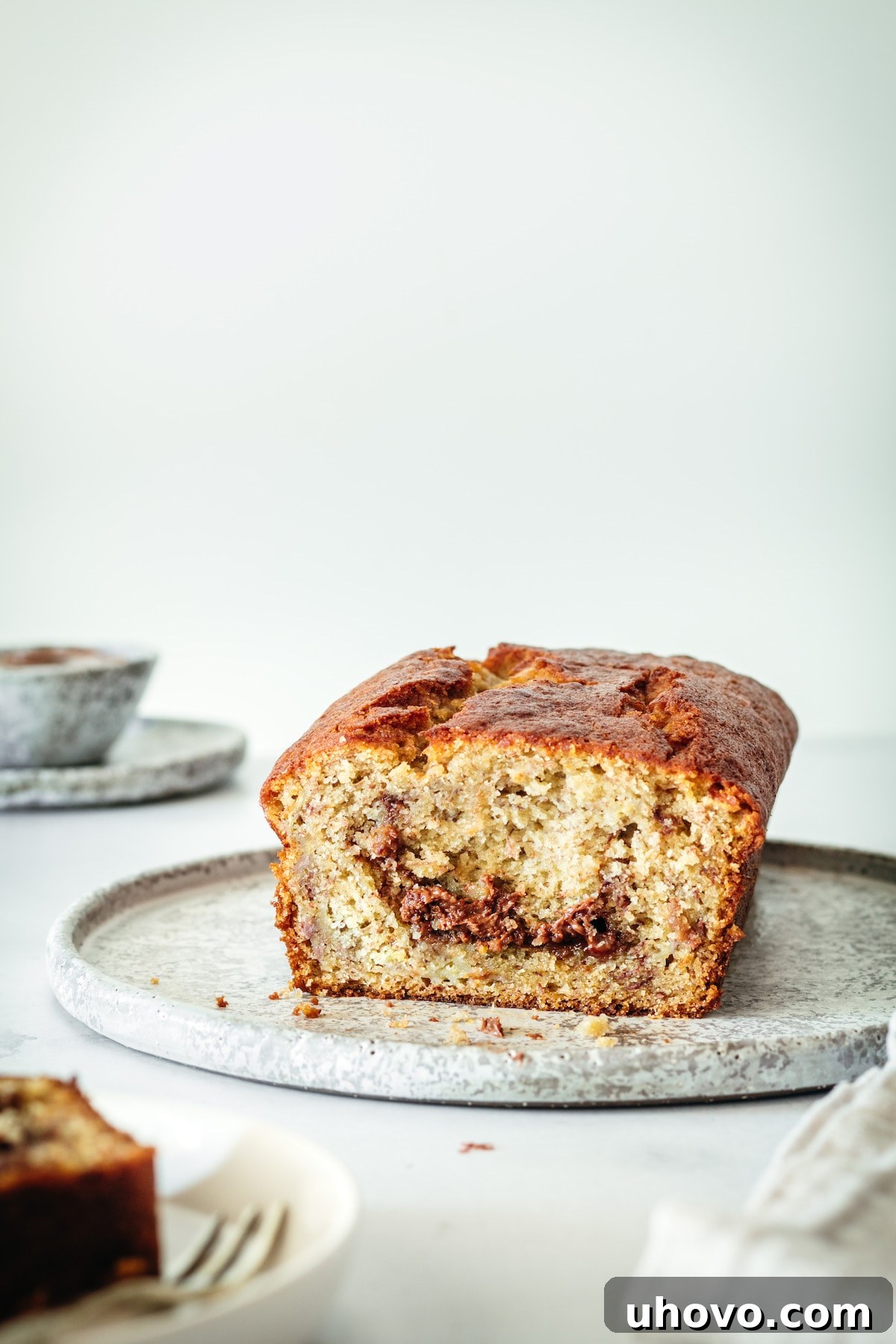 A freshly baked loaf of Nutella Banana Bread resting on a plate, cut open to reveal its moist interior and alluring, distinct Nutella swirls.