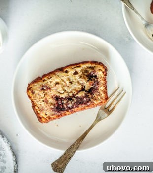 Overhead view of a delicious slice of Nutella Banana Bread on a plate with a fork, showcasing its rich Nutella swirls and inviting texture.
