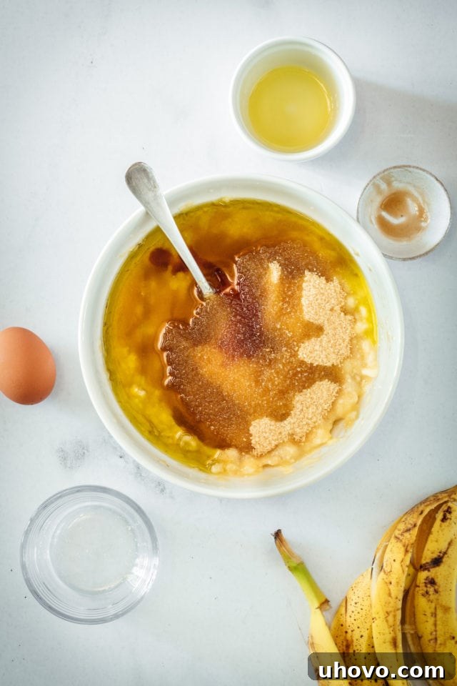 Overhead view of the fully combined wet ingredients for banana bread in a mixing bowl, featuring a smooth, uniform mixture with a spoon resting inside.