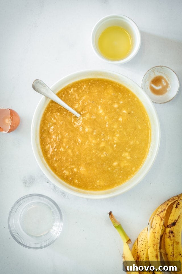 Close-up overhead view of the rich banana, sugar, oil, egg, and vanilla mixture in a mixing bowl, showing its thick, creamy texture, ready for dry ingredients.