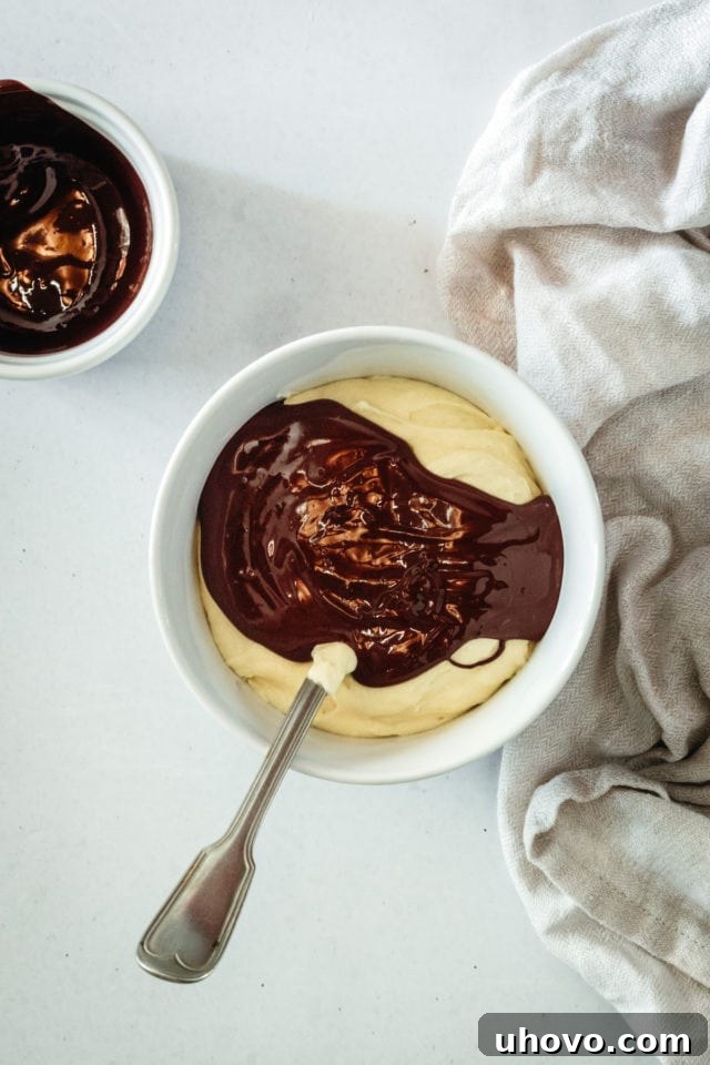 Overhead view of melted dark chocolate being gently mixed into a portion of the vanilla cake batter.