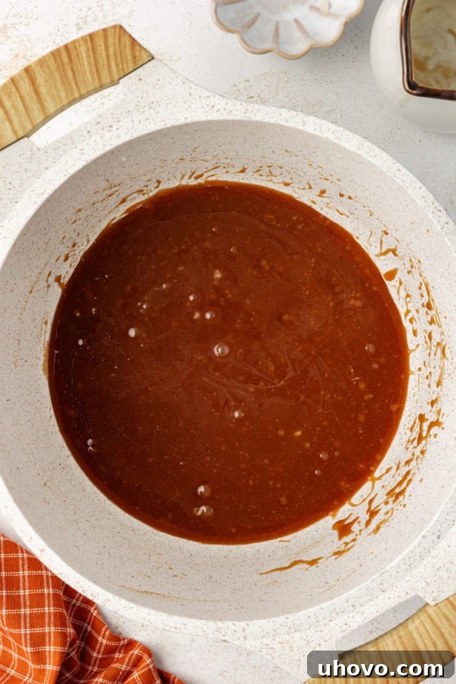 A rich, golden caramel sauce in a heat-proof bowl, after cream and butter have been stirred in, cooling to room temperature.