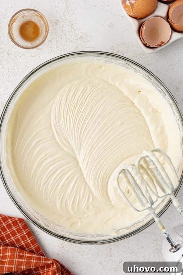 The cheesecake filling being mixed in a bowl with an electric mixer, showing the smooth consistency after eggs and vanilla have been incorporated.