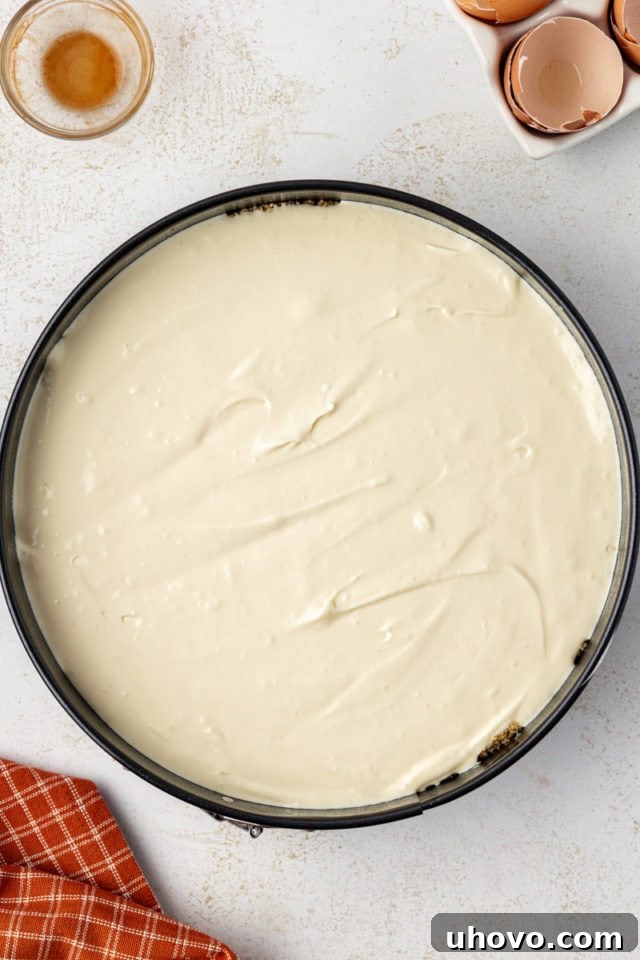 An unbaked cheesecake filling poured into the prepared graham cracker crust in a springform pan, ready for baking.