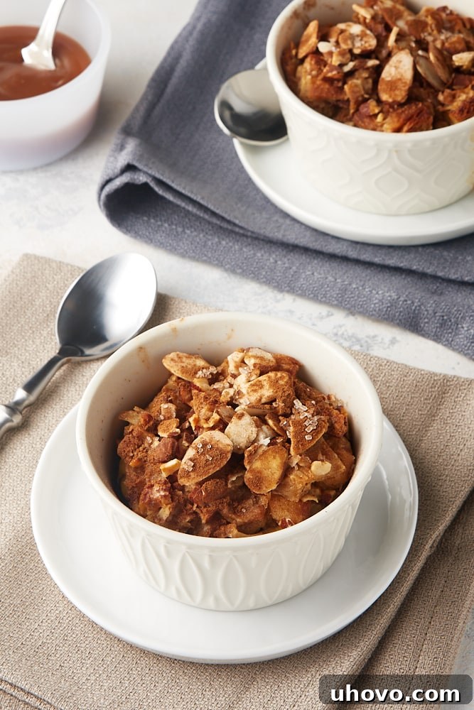 Cinnamon Almond Bread Pudding for Two in white ramekins on white plates on beige and gray napkins, garnished with salted caramel