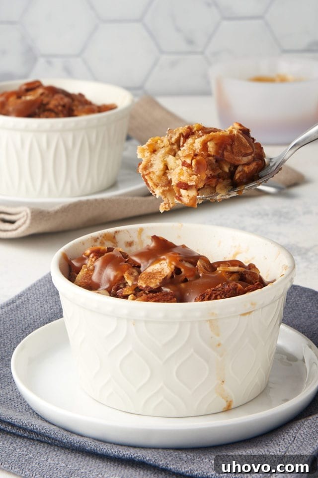 A bite of Cinnamon Almond Bread Pudding on a spoon held above the remaining bread pudding in a white ramekin, showing the creamy texture.