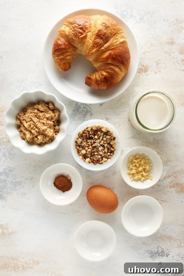 Overhead view of ingredients for Cinnamon Almond Bread Pudding for Two, including cubed croissants, almonds, almond paste, milk, brown sugar, an egg, and spices.