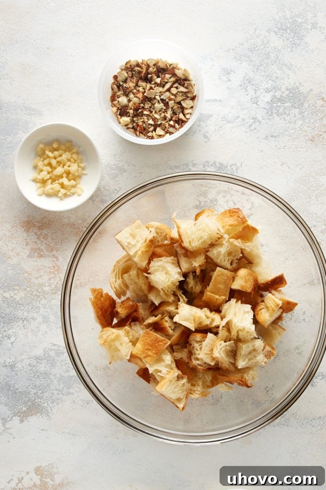Overhead view of cubed croissants, almond paste, and chopped almonds in separate bowls, ready for mixing.