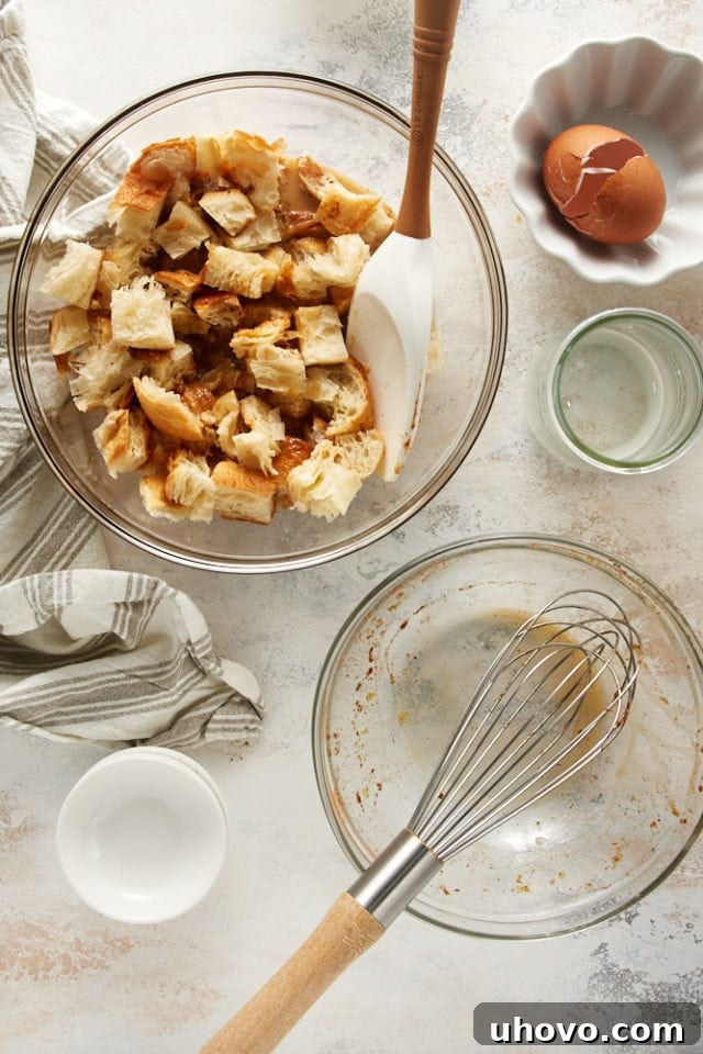 Overhead view of the combined Cinnamon Almond Bread Pudding for Two mixture in a glass bowl, surrounded by used mixing bowls.