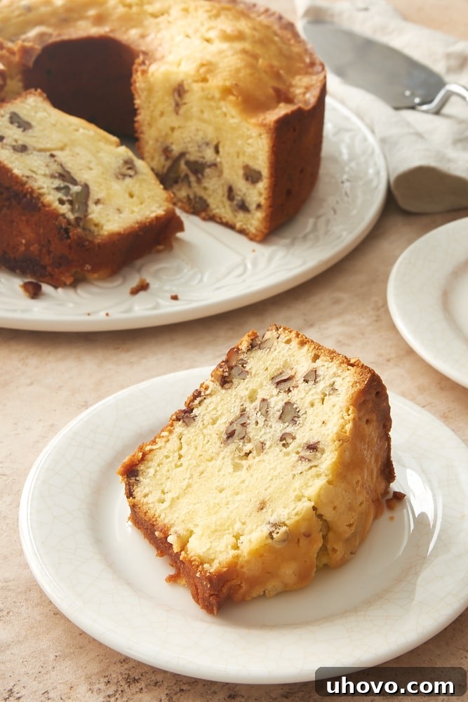 A perfectly sliced piece of Cream Cheese Pecan Pound Cake on a white plate, showcasing its moist texture and pecan pieces.