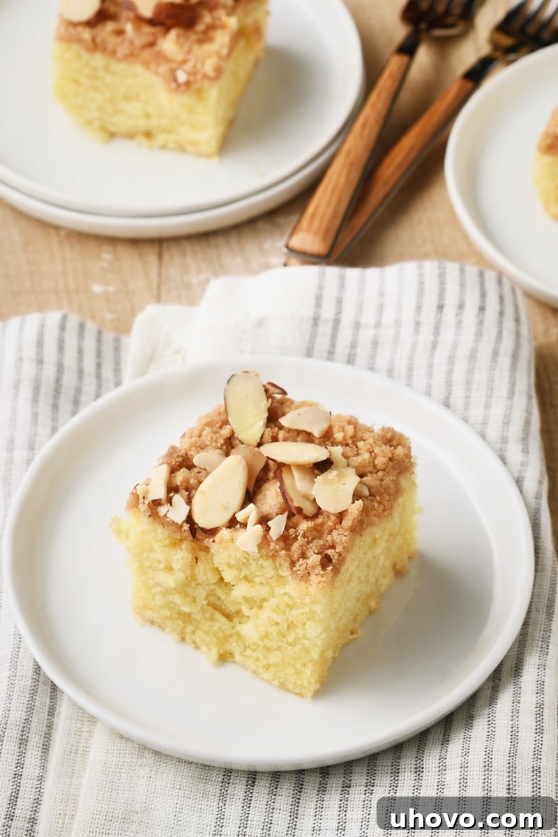 A perfectly baked slice of Almond Crumb Cake on a round white plate, ready to be enjoyed.