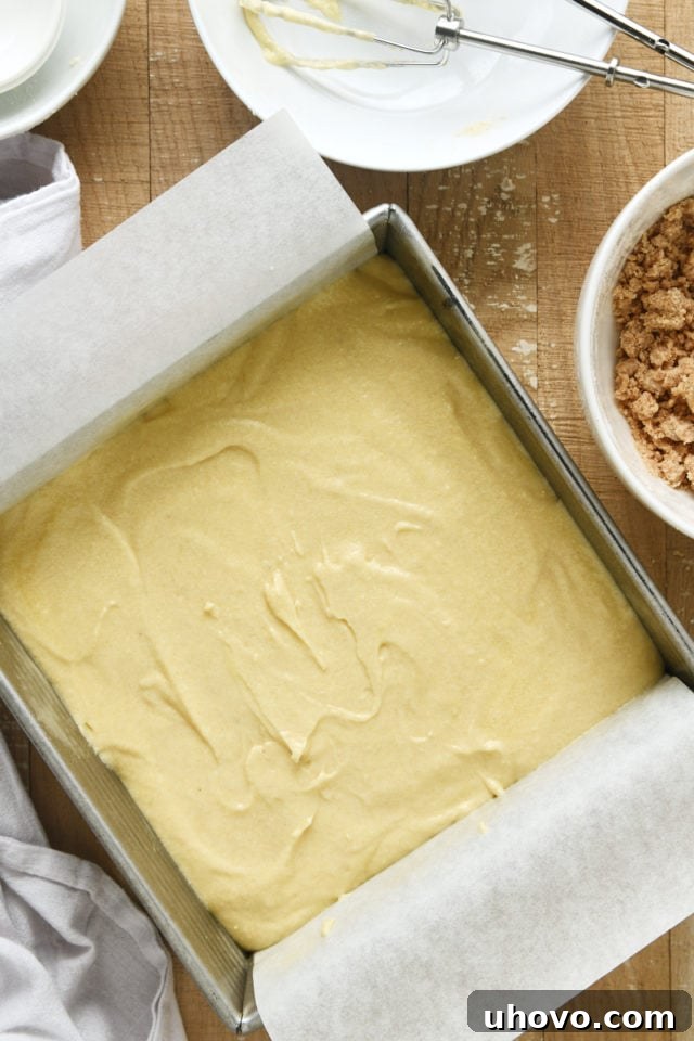 Overhead view of Almond Crumb Cake batter spread evenly in a parchment-lined square baking pan.