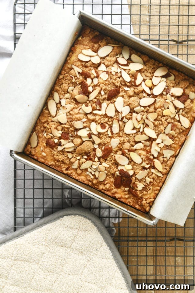 Overhead view of a freshly baked Almond Crumb Cake cooling on a wire rack, steam gently rising.