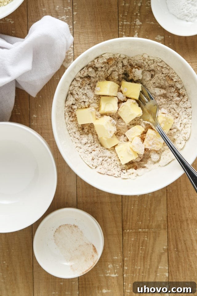 Overhead view of cubed unsalted butter being added to the dry crumb topping ingredients in a white mixing bowl.