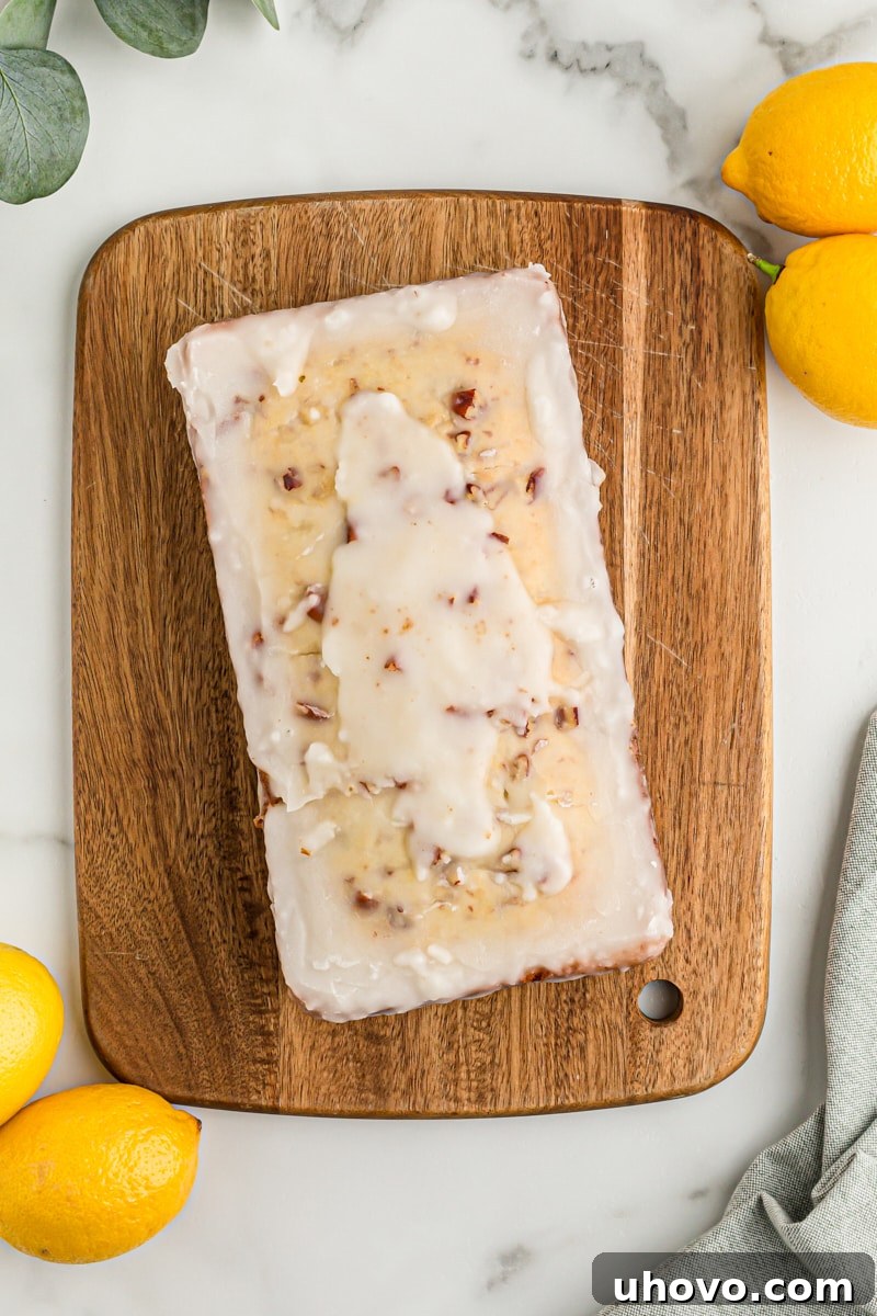 Overhead view of glazed lemon bread on wood board with lemons