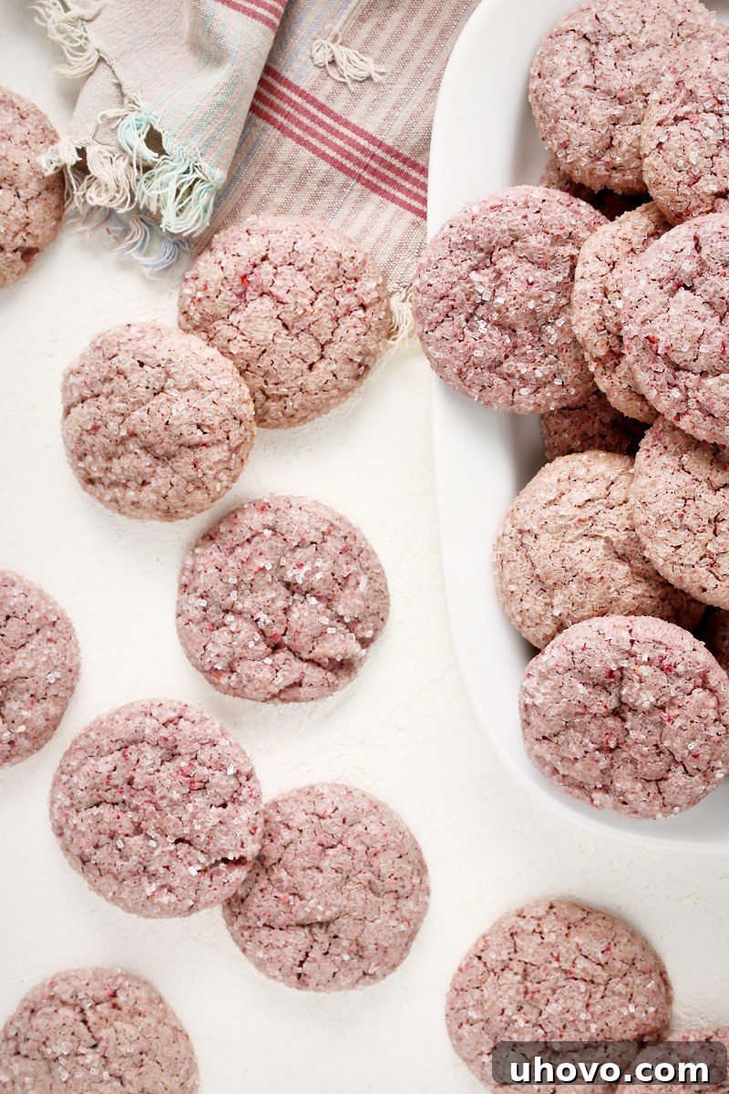 Overhead view of raspberry sugar cookies scattered on a white surface and beautifully piled on a white tray, ready to be enjoyed.