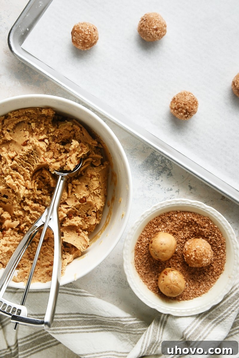 overhead view of Brown Butter Cinnamon Cookies being shaped, rolled in cinnamon-sugar, and placed on a baking sheet