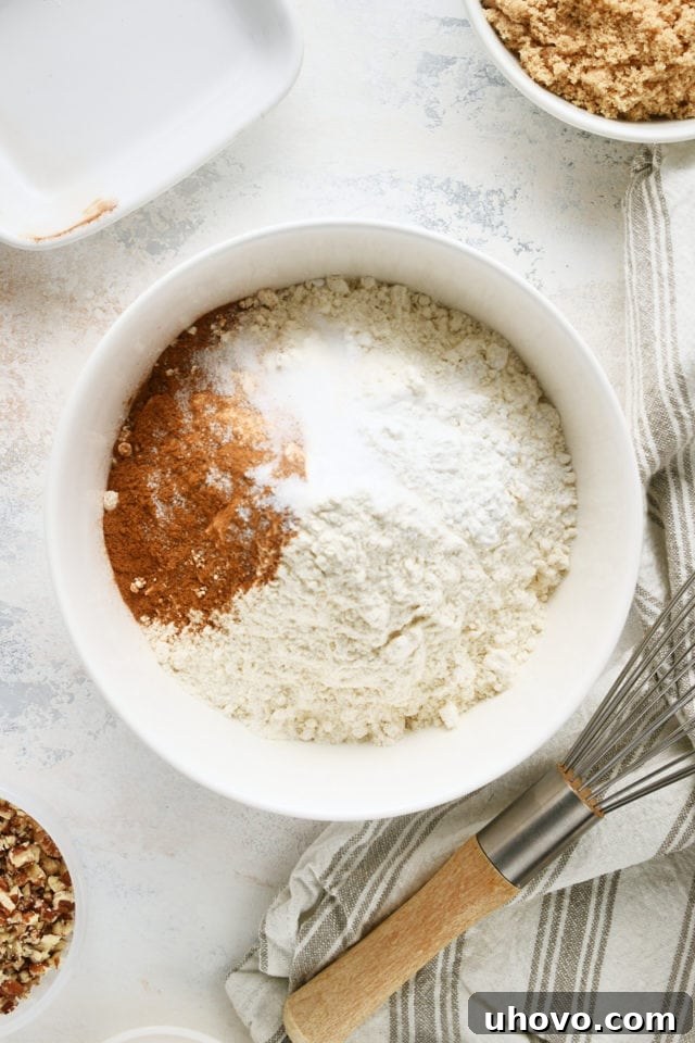 overhead view of flour, baking powder, baking soda, salt, and cinnamon in a white mixing bowl