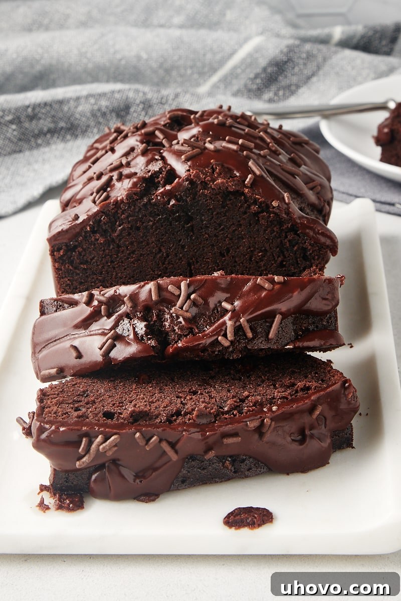 A perfectly sliced Chocolate Loaf Cake, drizzled with a rich chocolate glaze, presented beautifully on a white serving tray, tempting anyone who loves chocolate.